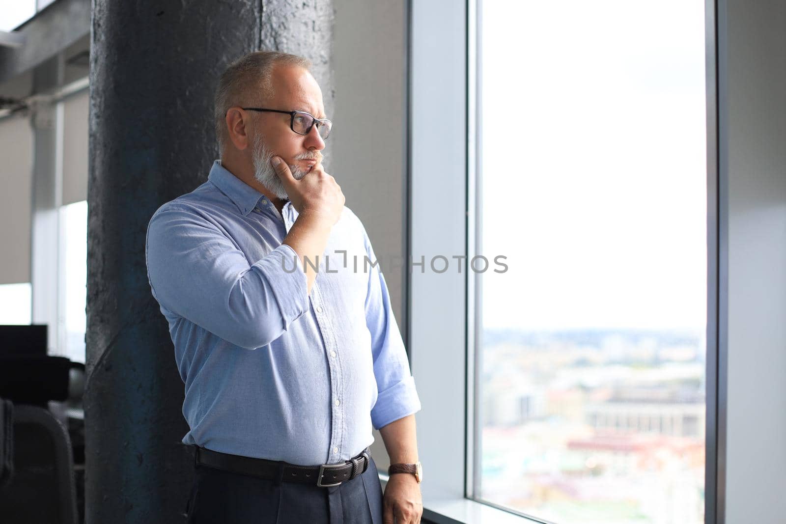 Thoughtful mature business man in a corporate suit looking away while standing near the window