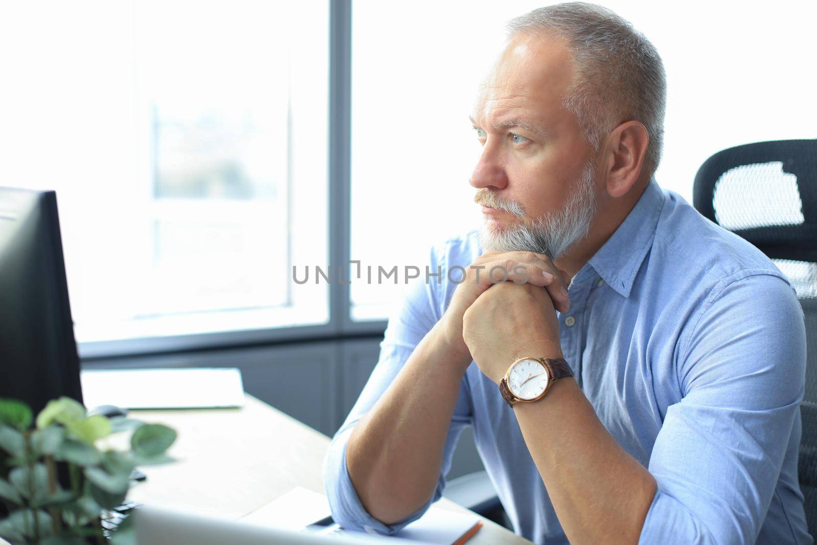 Focused mature businessman deep in thought while sitting at a table in modern office. by tsyhun