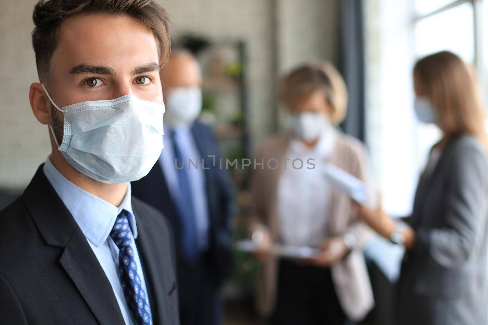 Businessman in medical mask with colleagues in the background in office