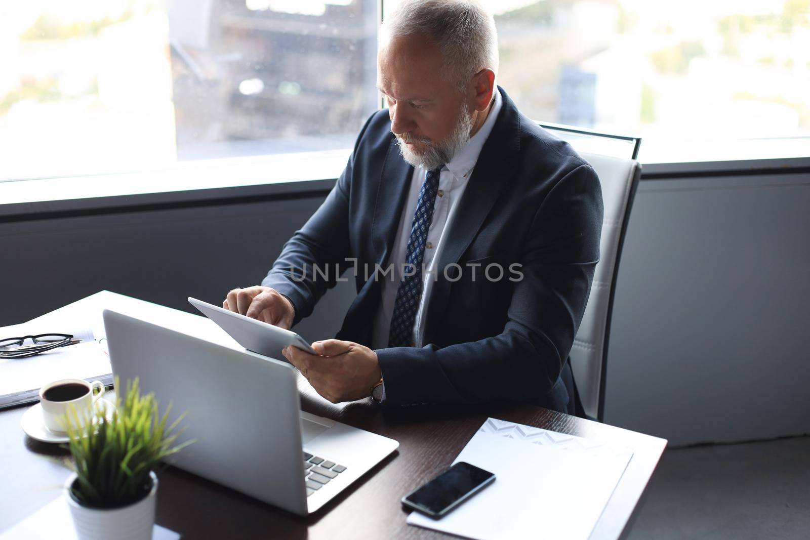 Mature business man in full suit using digital tablet while sitting in the office. by tsyhun