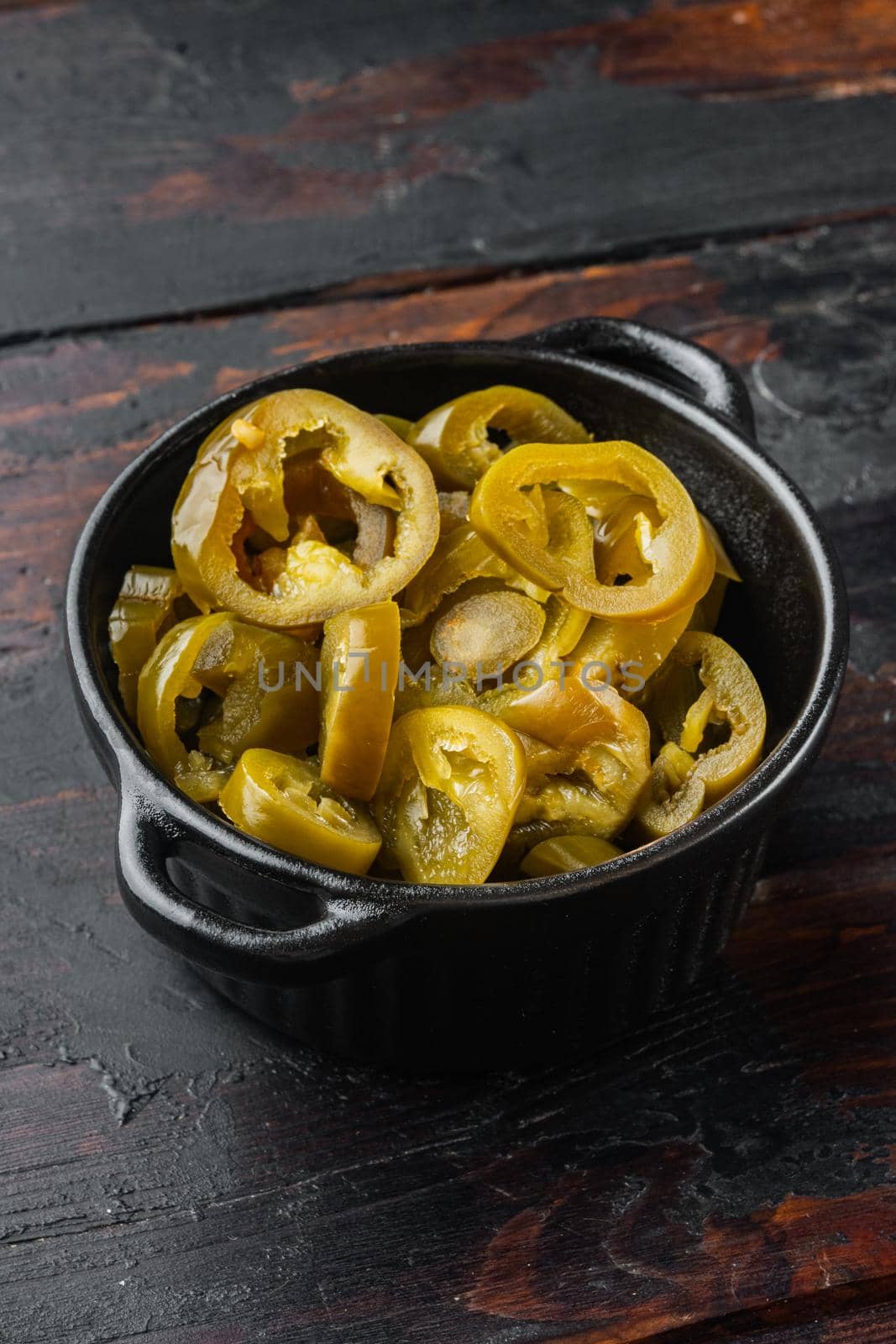 Slices of preserved Jalapeno peppers, on old dark wooden table background