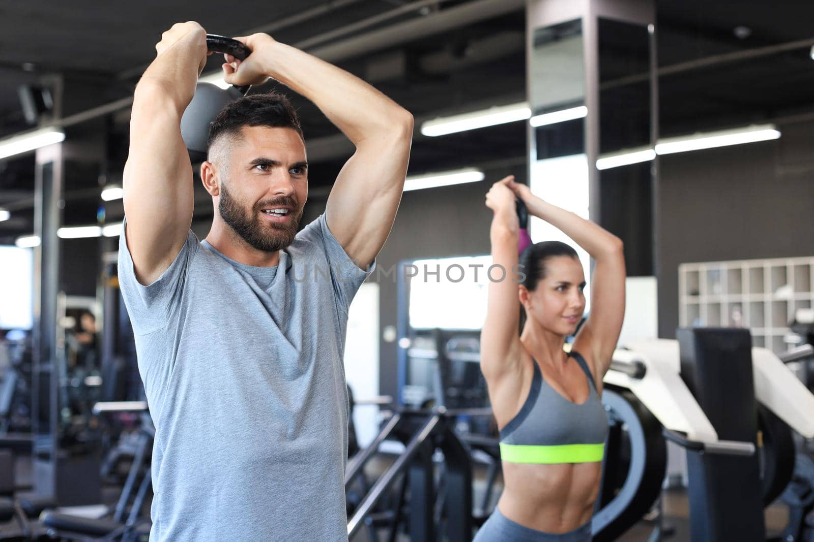 Fit and muscular couple focused on lifting a dumbbell during an exercise class in a gym. by tsyhun