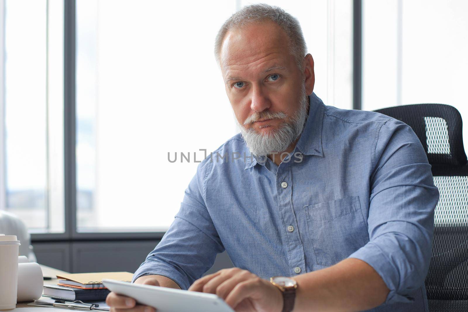 Mature businessman working using digital tablet while sitting in the modern office. by tsyhun