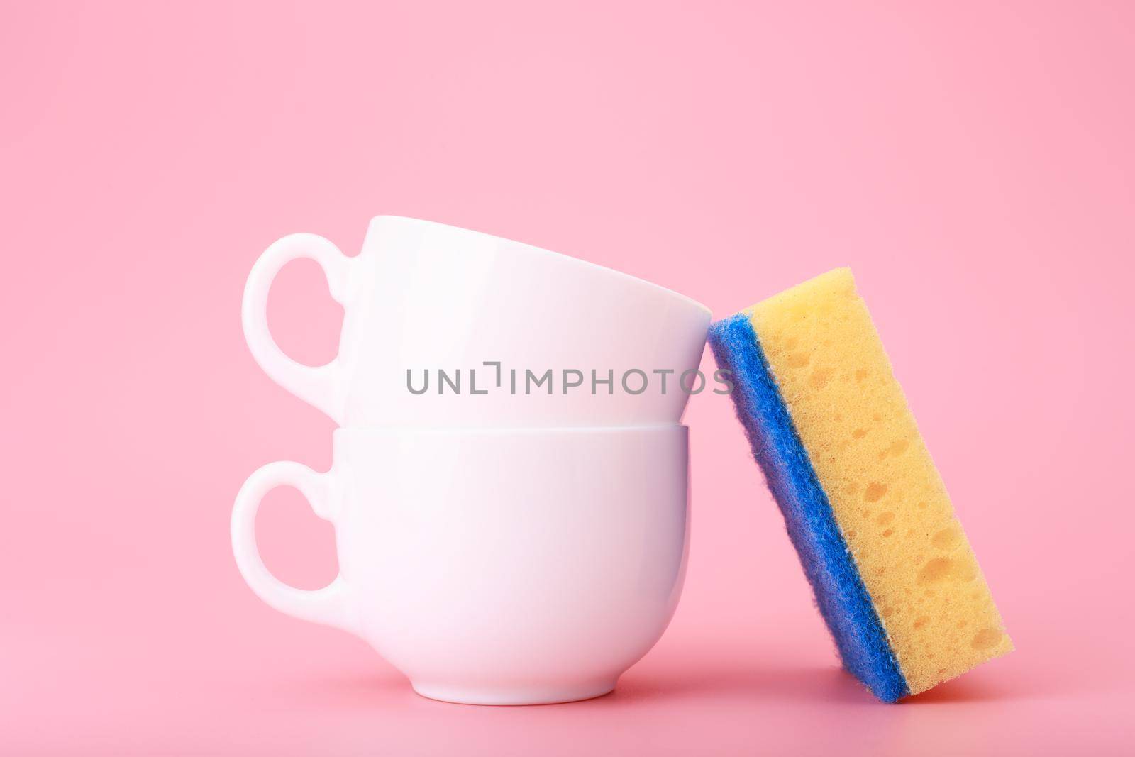Creative, minimal dishwashing concept, yellow cleaning sponge next to two white ceramic cups on pink background by Senorina_Irina