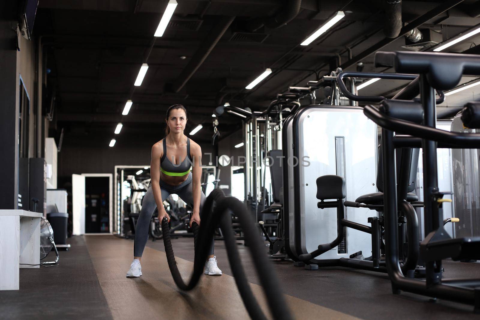 Fit woman using battle ropes during strength training at the gym