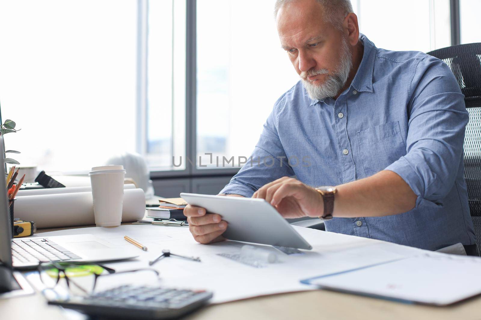 Mature businessman working using digital tablet while sitting in the modern office