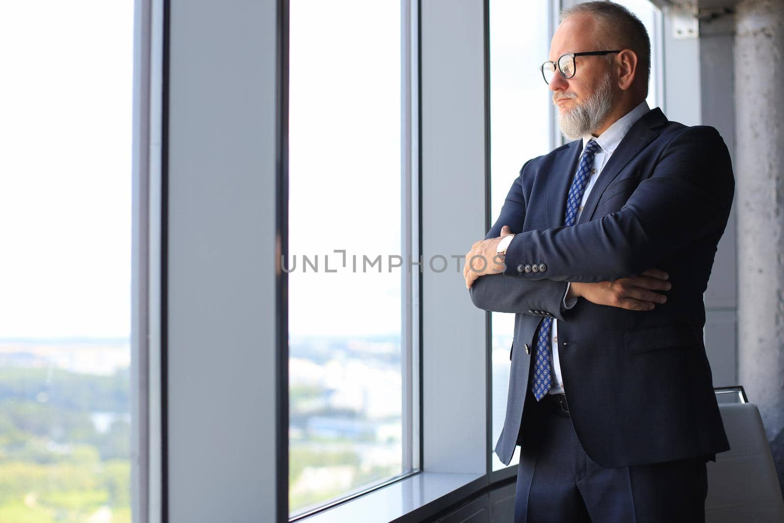 Thoughtful mature business man in full suit looking away while standing near the window