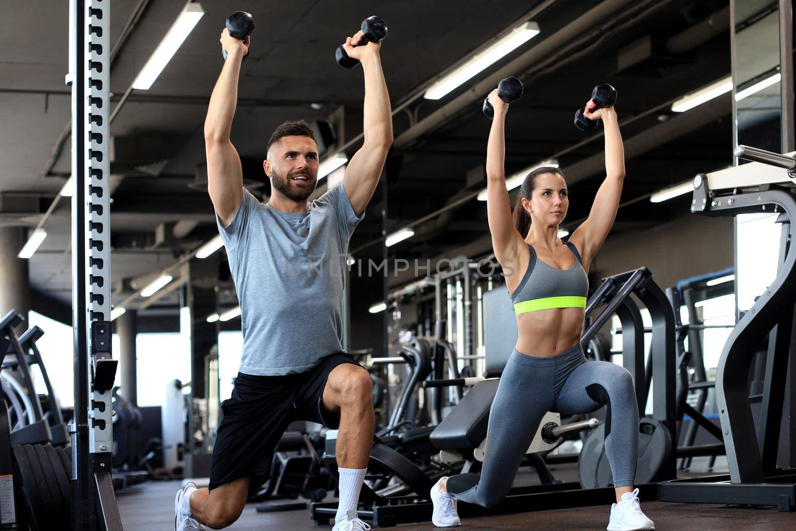 Attractive sports people are working out with dumbbells at gym