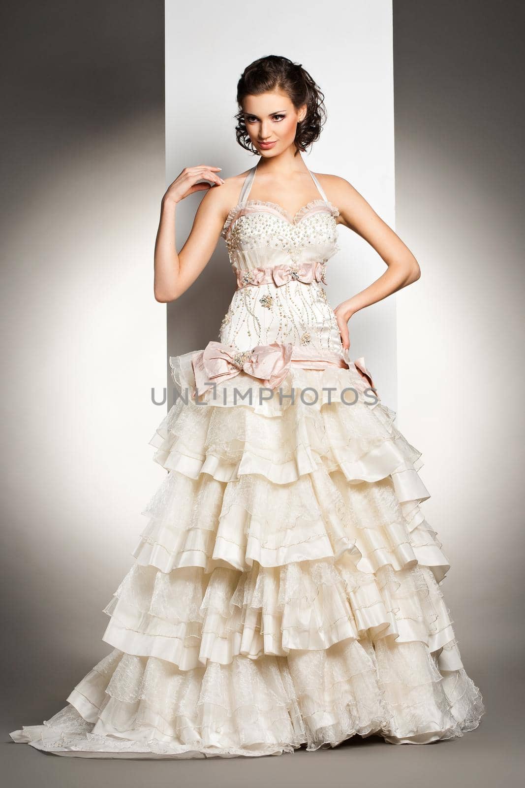 The beautiful young woman posing in a wedding dress over grey backround