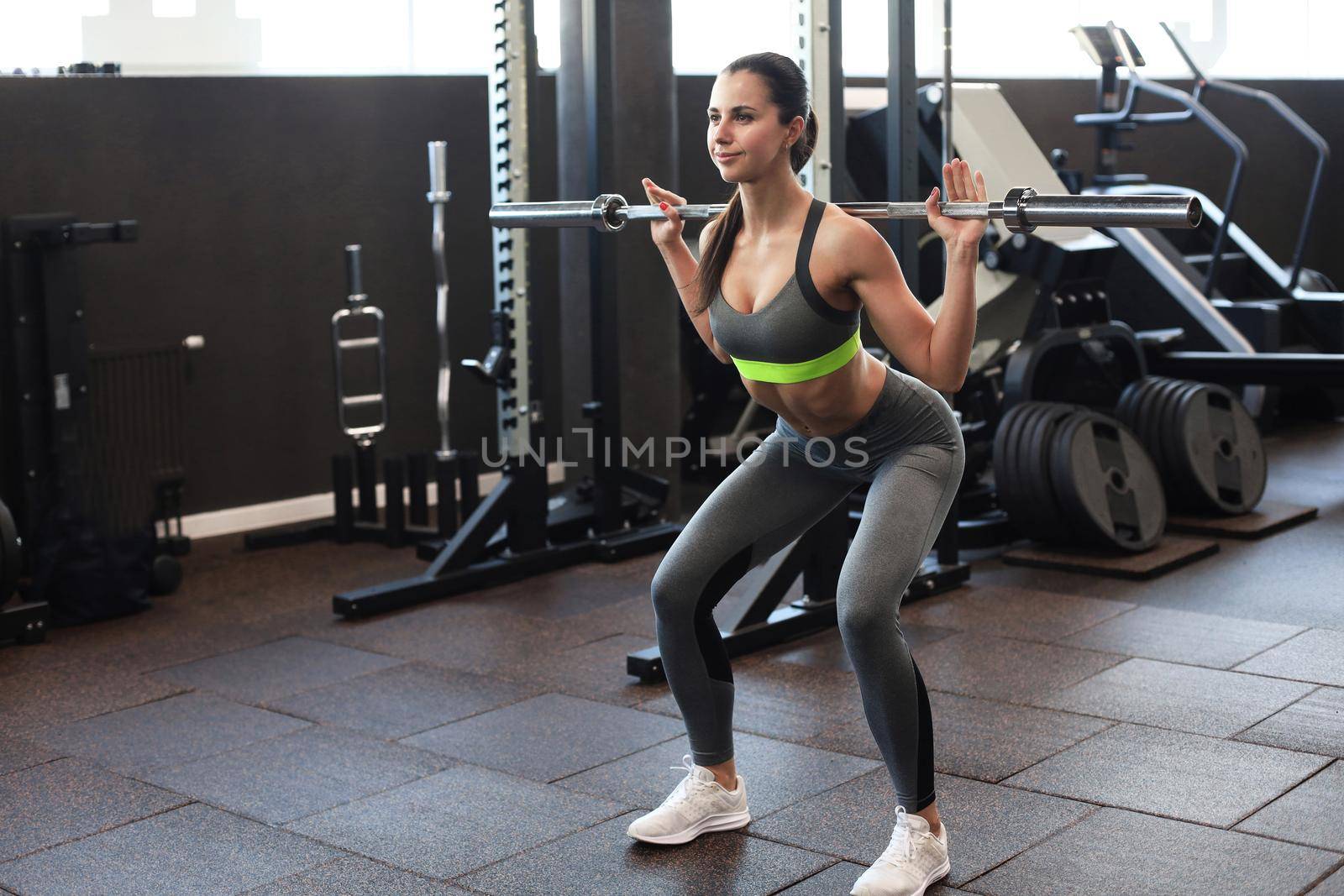 Muscular woman working out in gym doing exercises with barbell at biceps