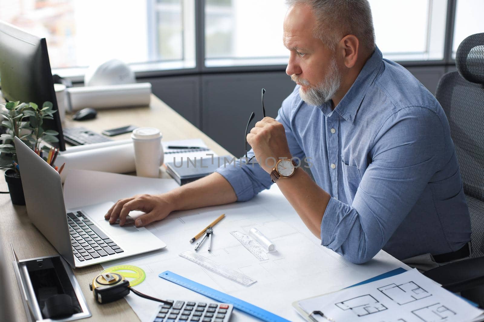 Senior businessman with a stylish short beard working on laptop computer at his office desk. by tsyhun