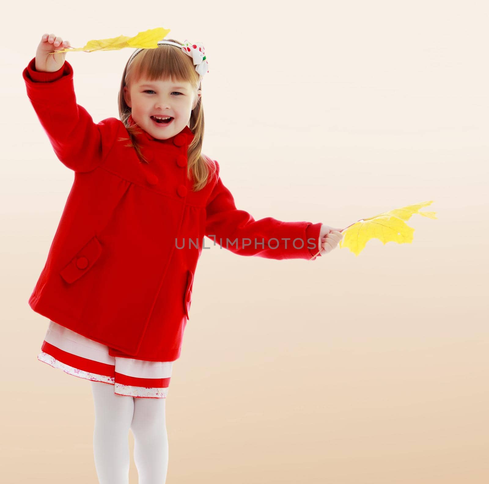 Girl enjoys the autumn weather. On a brown background. Joyful little girl in a bright red coat waving yellow maple leaves.