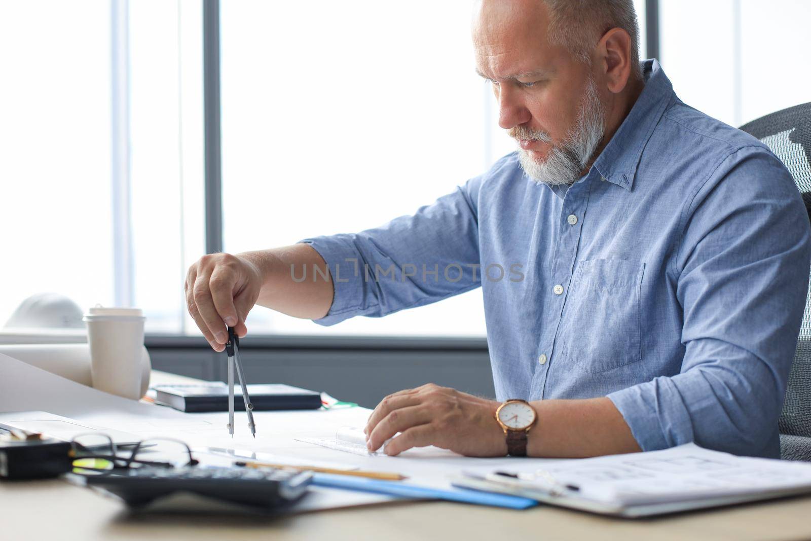 Concentrated mature business man working with drawing compass while sitting in the modern working space