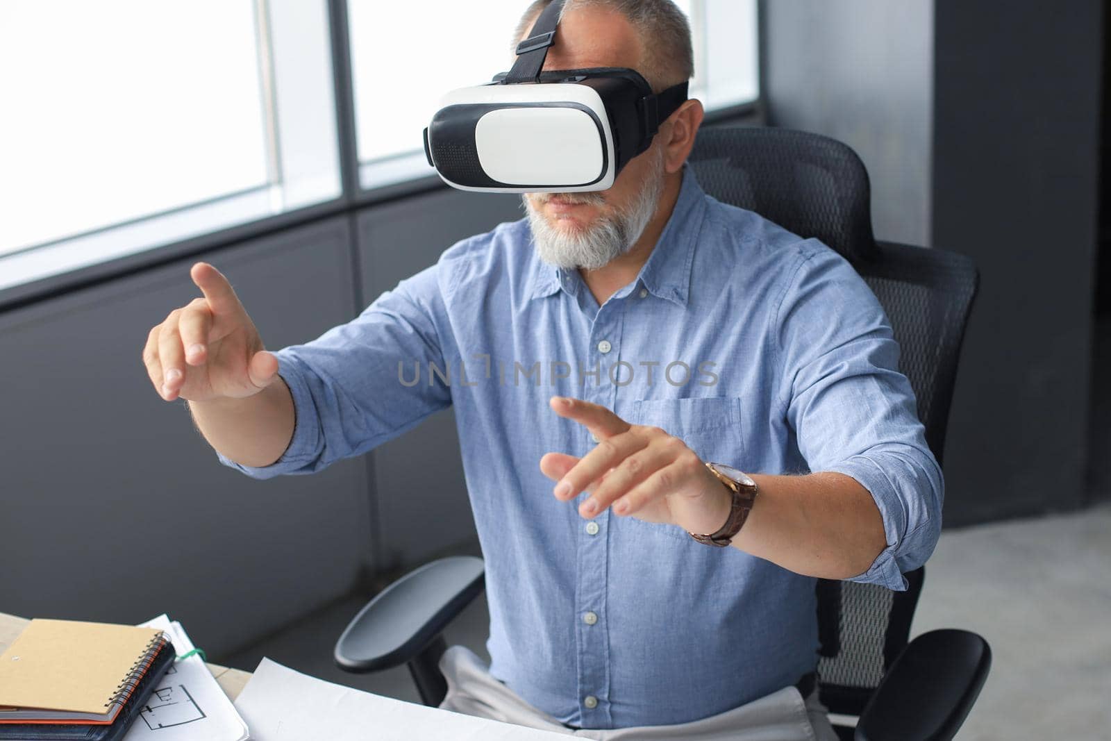 Mature businessman wearing a VR headset while sitting in modern office. Change the way you see and experience the world. by tsyhun