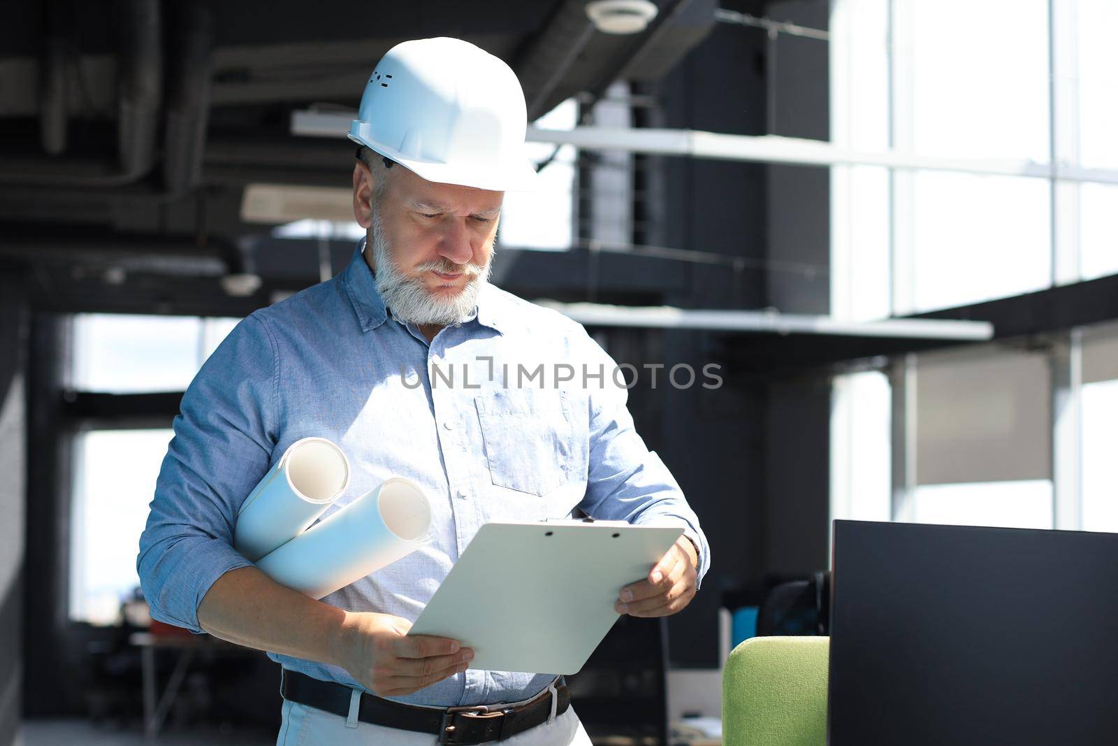 Mature architect wearing hardhat inspecting new building. by tsyhun