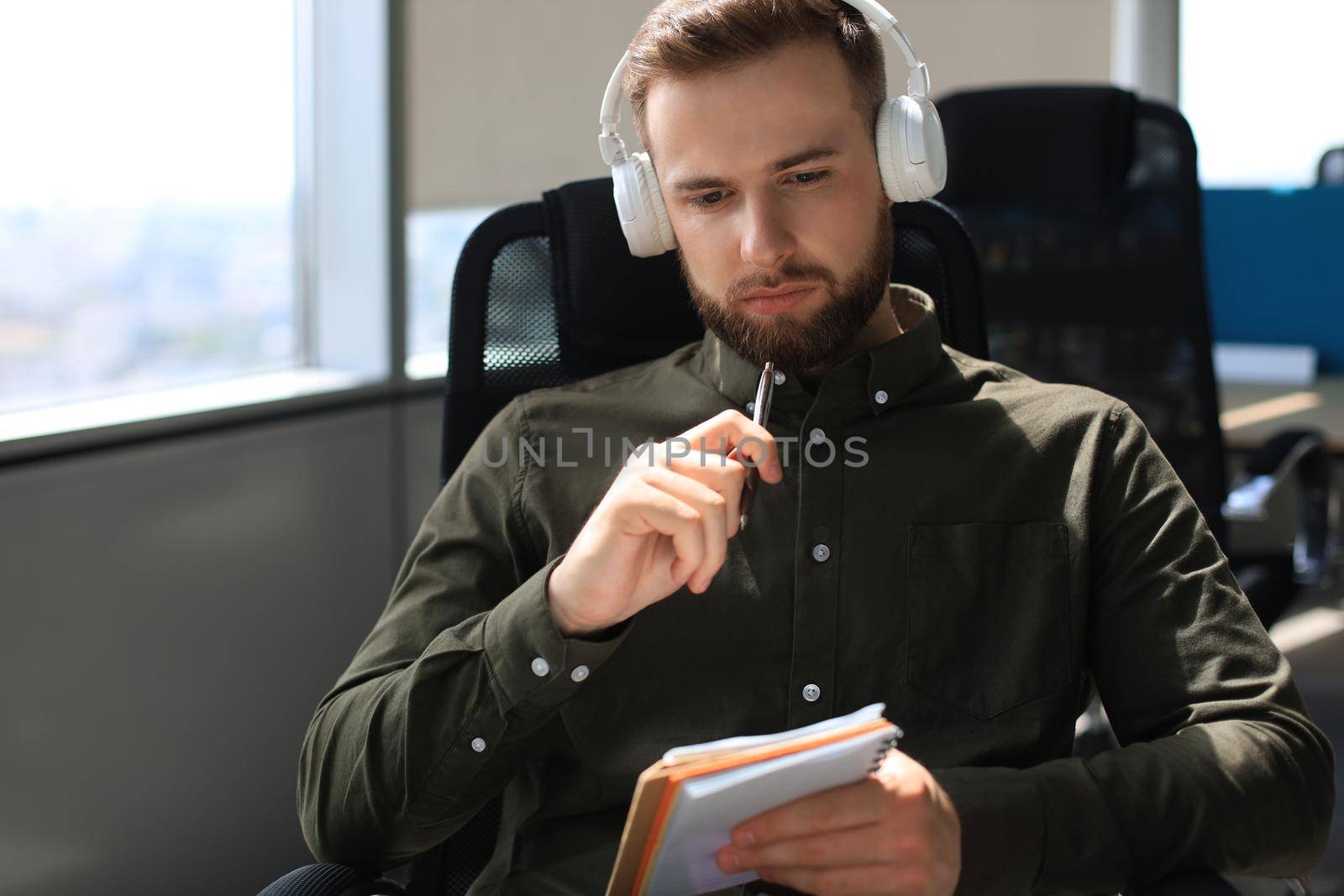 Thoughtful young business man writing something down while working in modern office