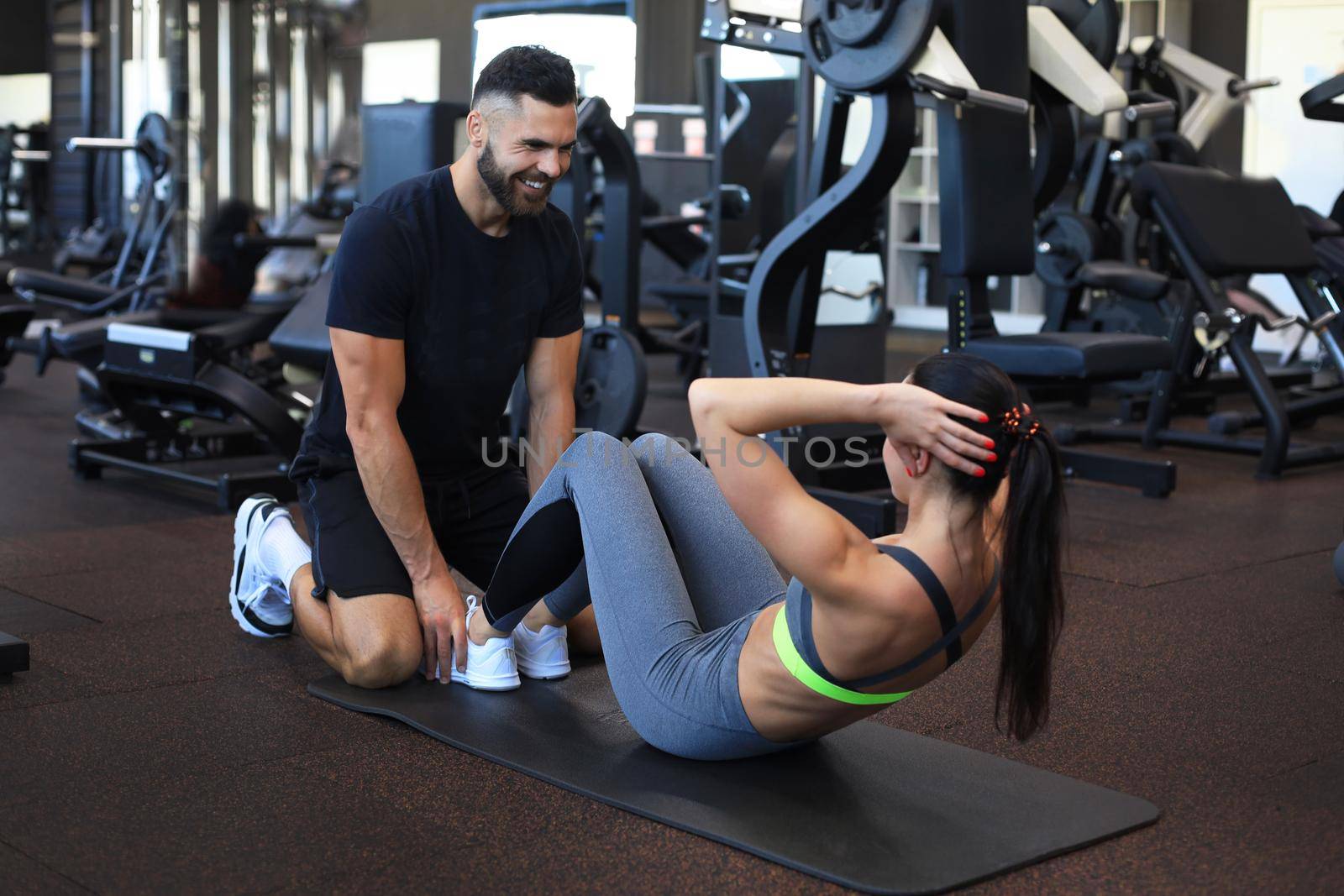 Trainer helping young woman to do abdominal exercises in gym