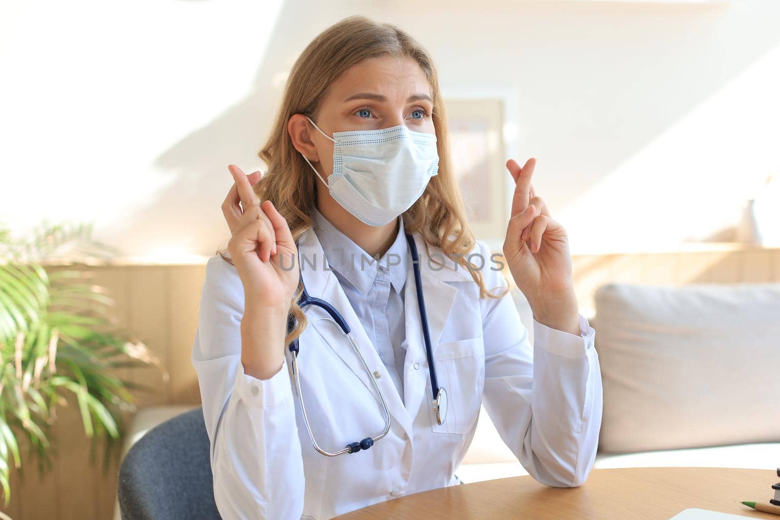 Female doctor with fingers crossed sitting in medical office