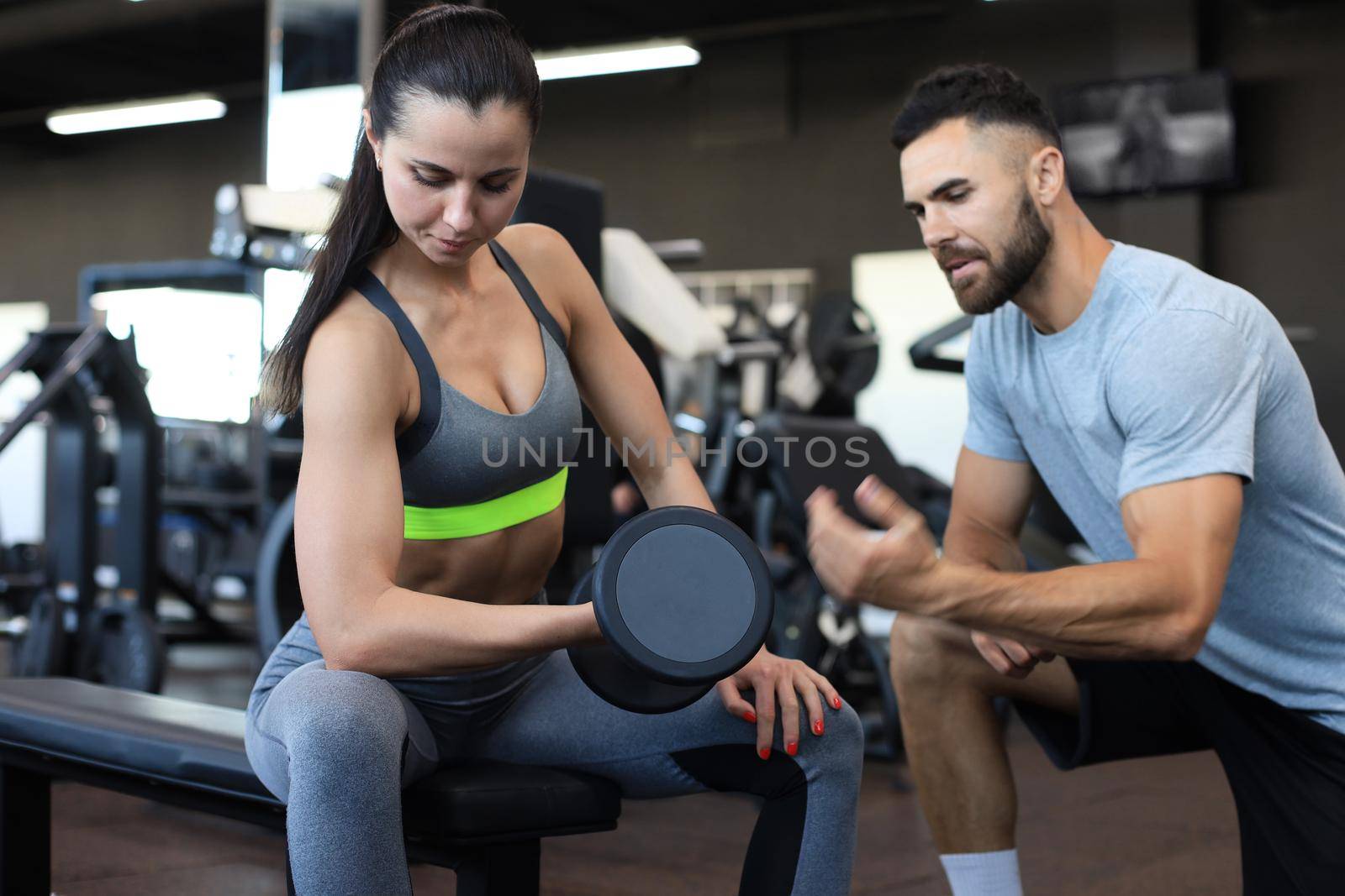 Beautiful woman doing an exercise with weight the guidance of a coach in gym