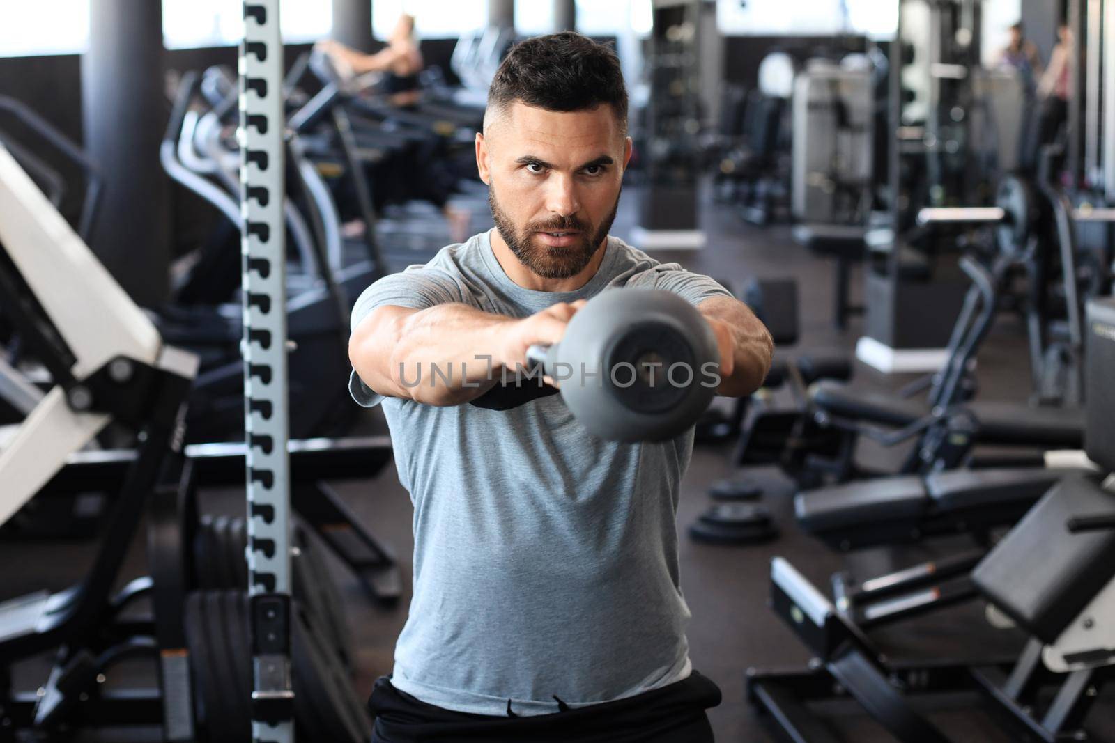 Fit and muscular indian man focused on lifting a dumbbell during an exercise class in a gym