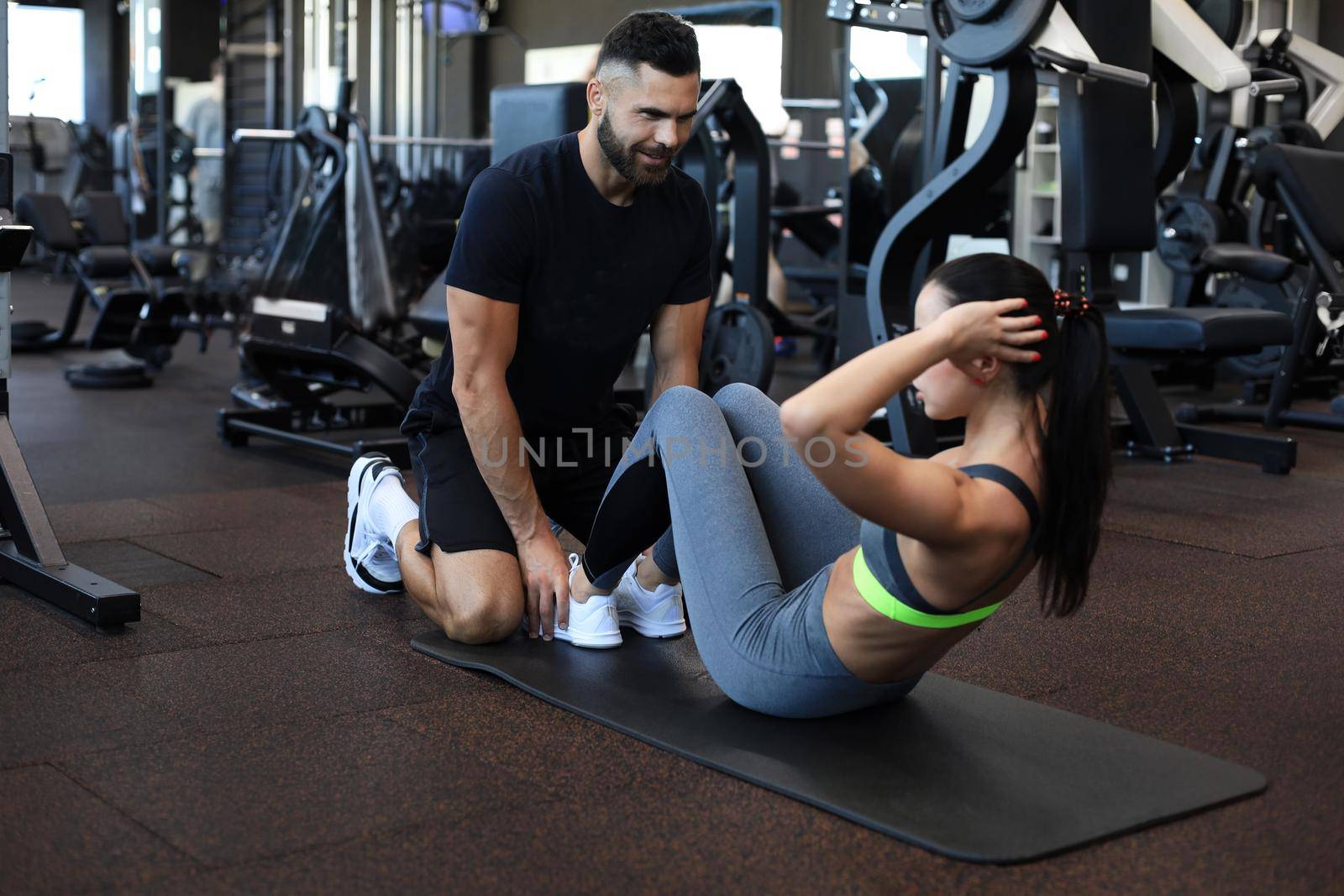 Trainer helping young woman to do abdominal exercises in gym. by tsyhun