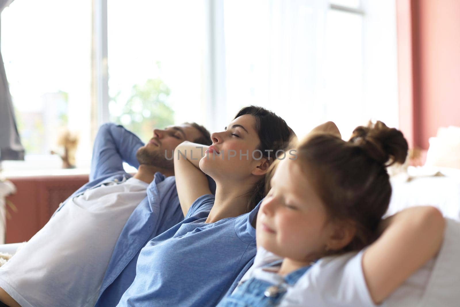 Relaxed young family resting and dreaming about new home on comfortable sofa together at home, happy young parents with little daughter relax enjoying nap relaxing or meditating