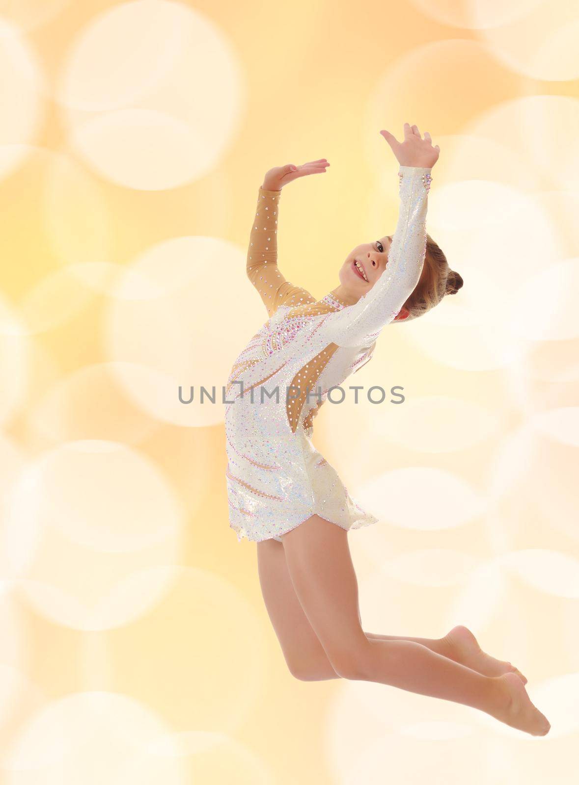 Beautiful little girl gymnast dressed in sports swimsuit, jumps high.On blurred brown background with white Christmas snowflakes.