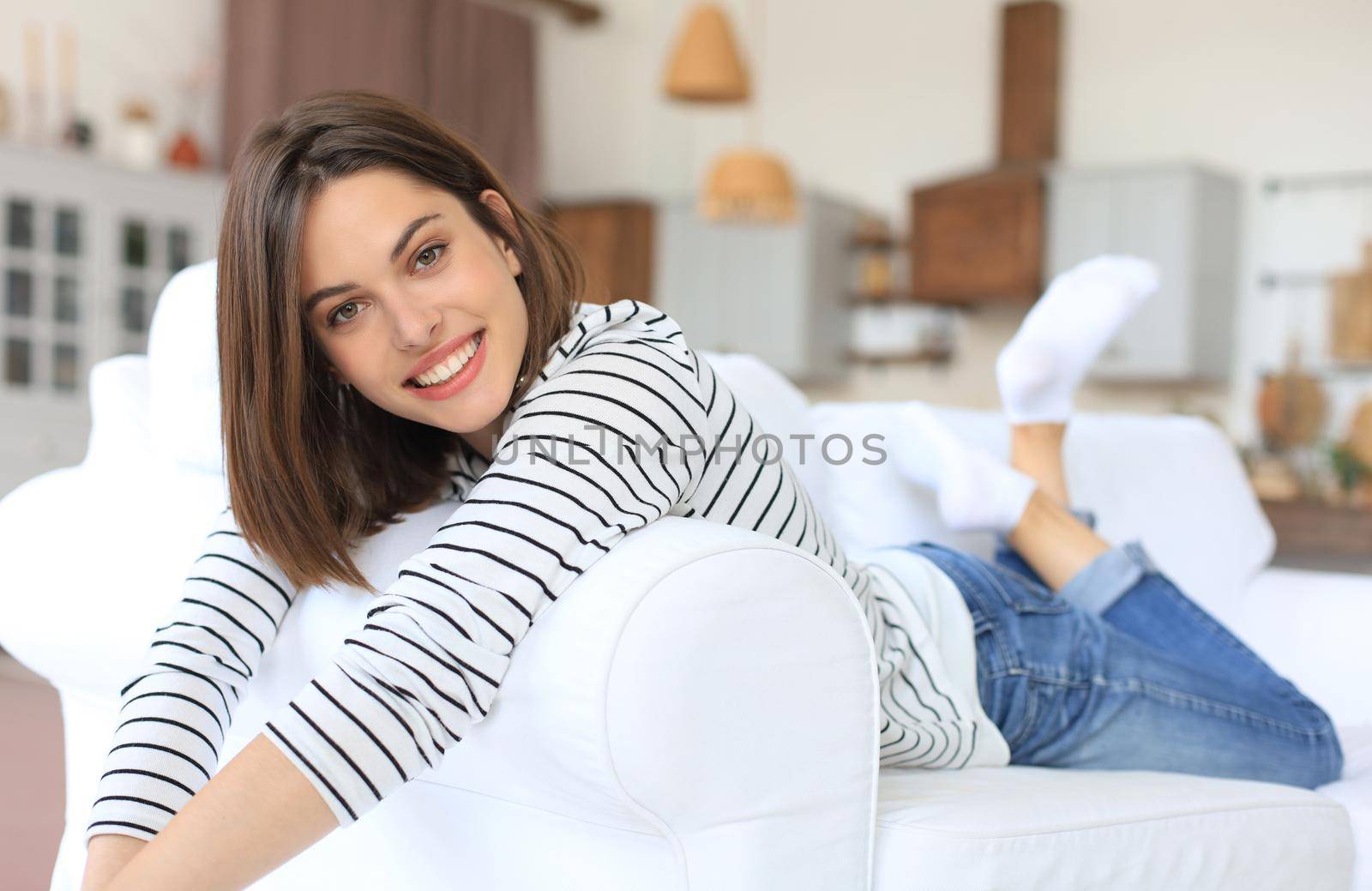 Smiling woman crossing her arms while lying on a sofa in living room. by tsyhun