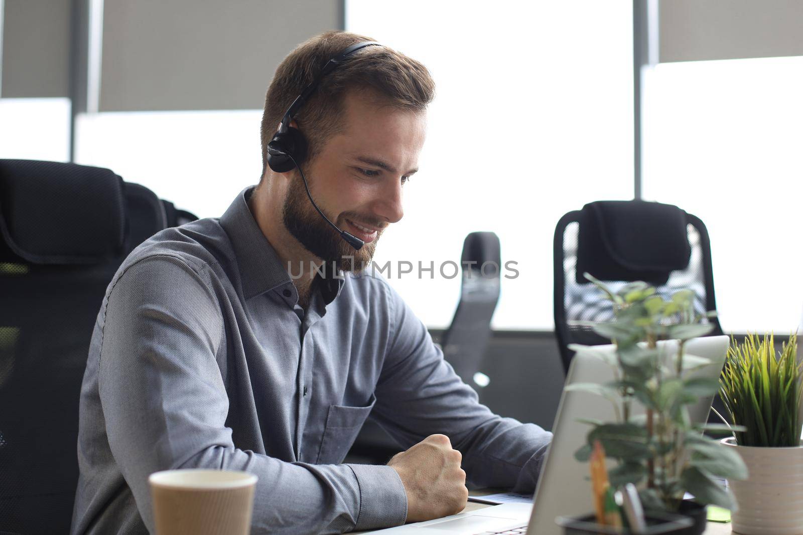 Smiling male business consultant with headphones sitting at modern office, video call looking at laptop screen. Man customer service support agent helpline talking online chat. by tsyhun