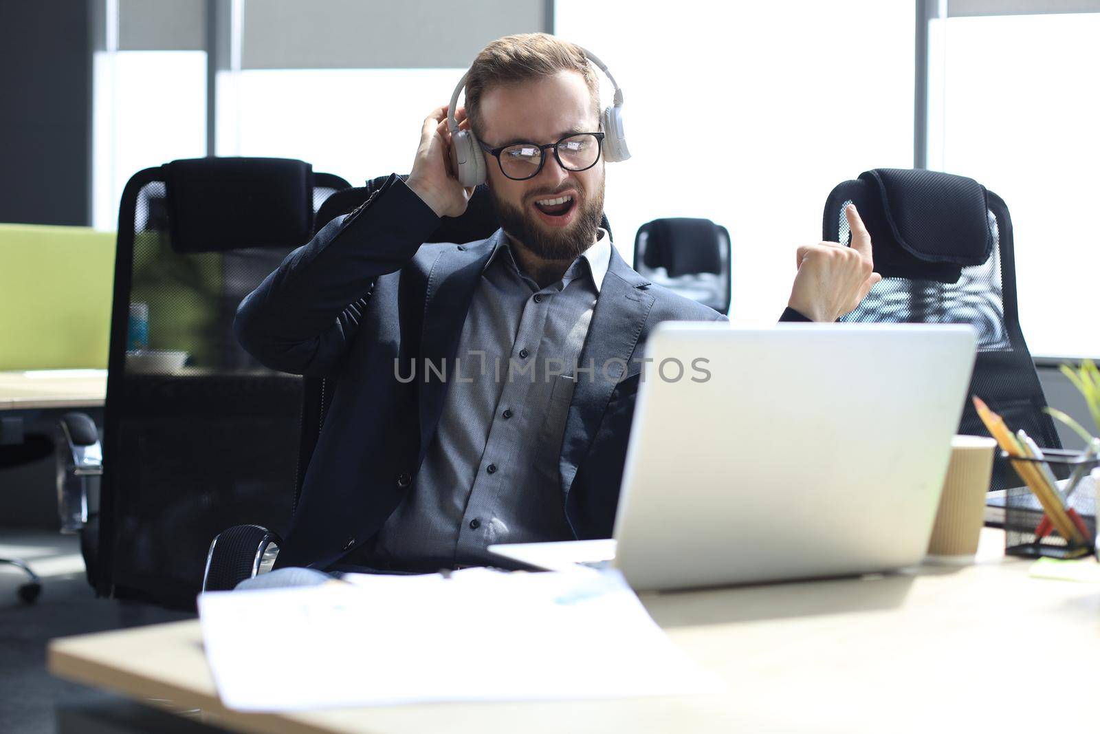 Smiling handsome businessman relaxing and listening music in earphones in a modern office