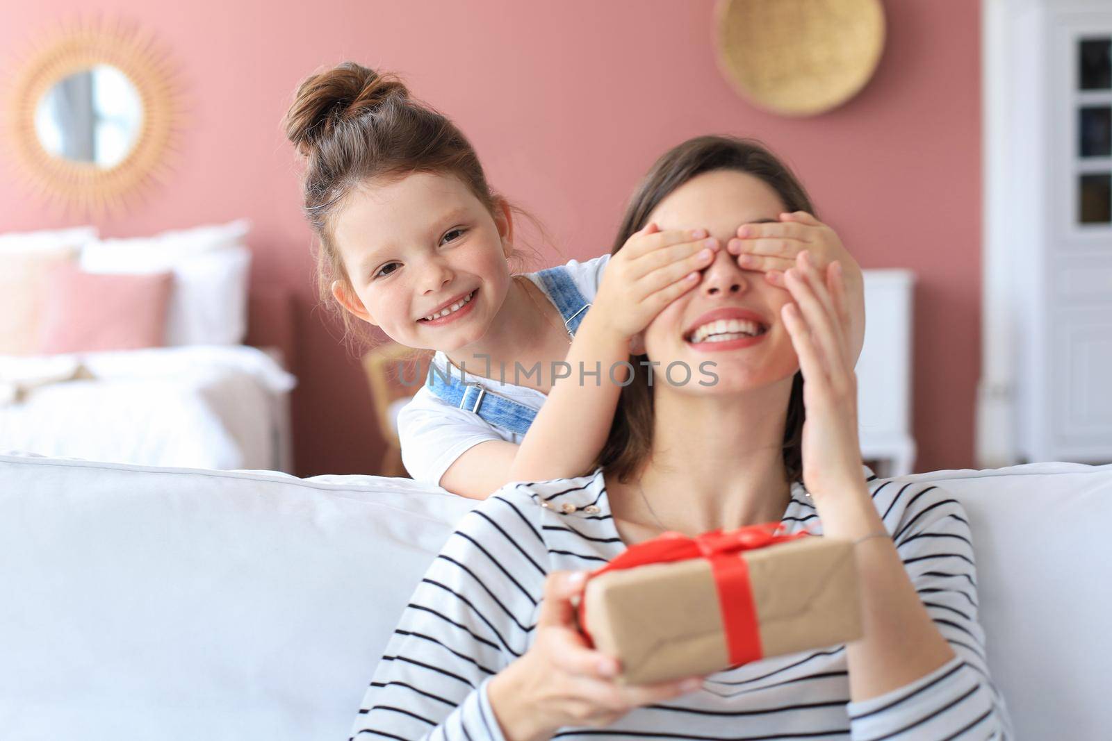 Little girl make birthday present to excited parent , smiling little child congratulate give gift box to happy mother and closed mother's eyes