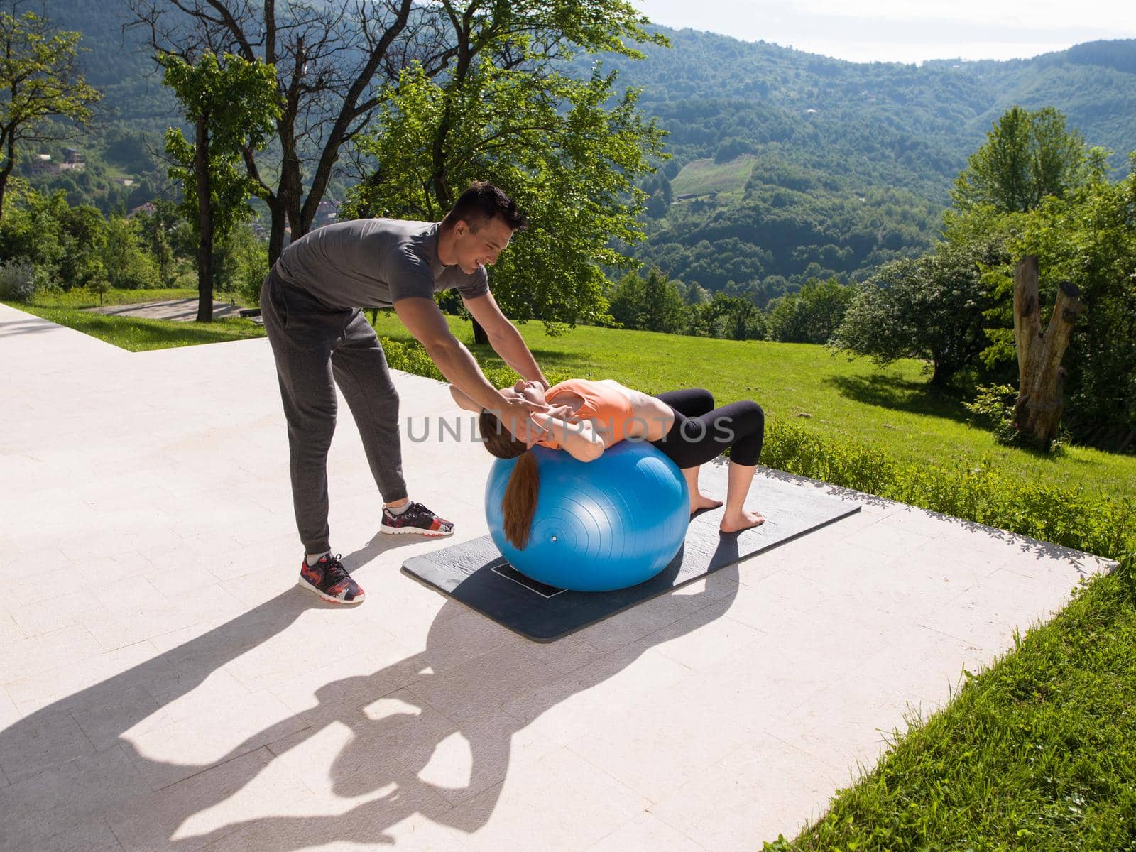 young beautiful woman and personal trainer doing exercise with pilates ball in front of her luxury home