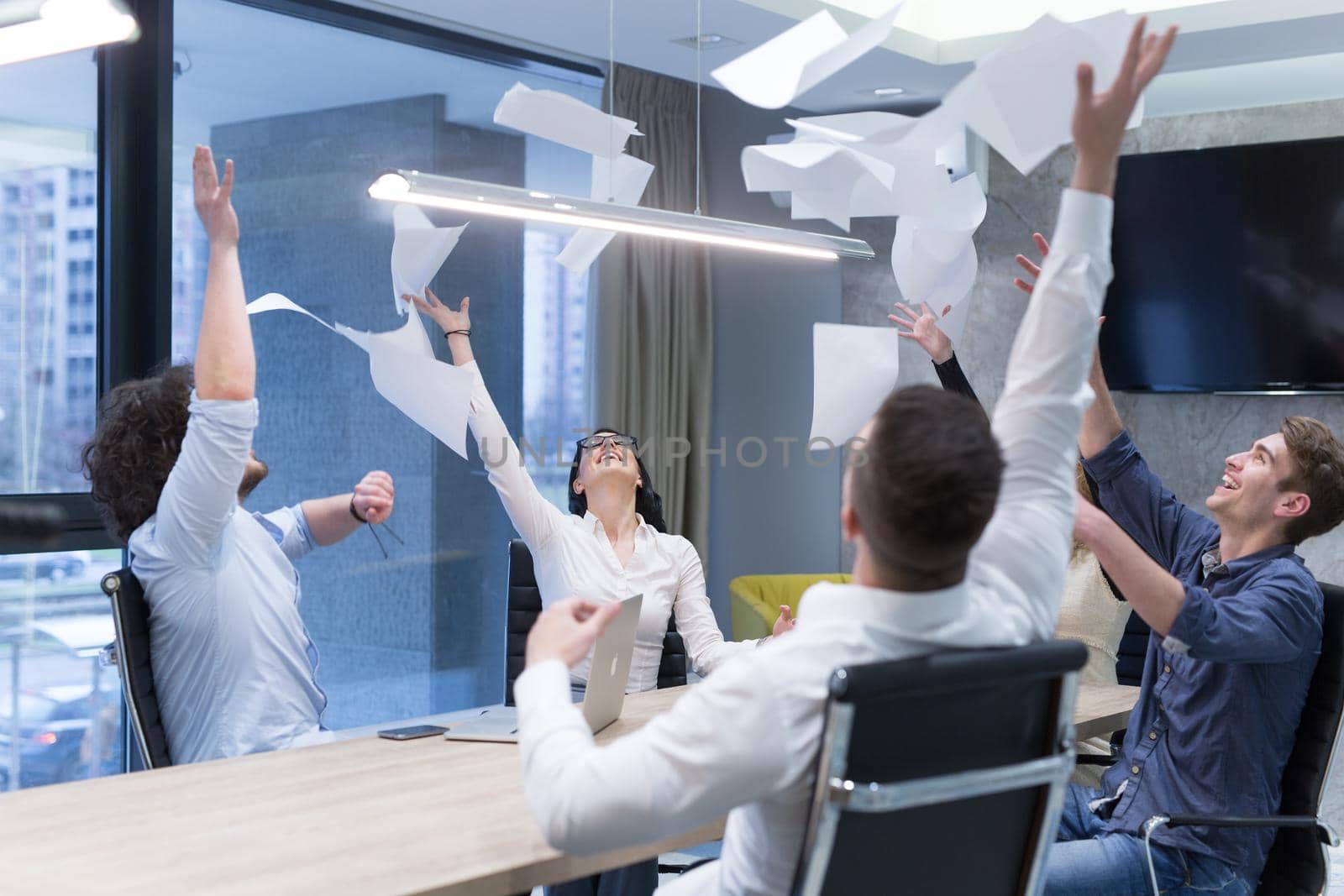 Group of young business people throwing documents and looking happy while celebrating success at their working places in startup office