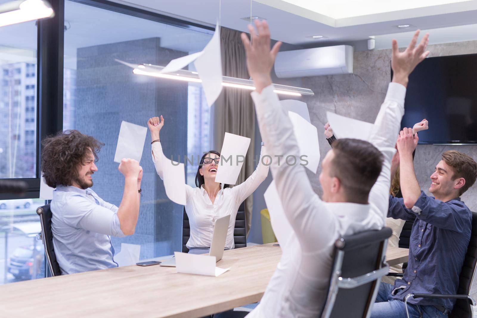 Group of young business people throwing documents and looking happy while celebrating success at their working places in startup office