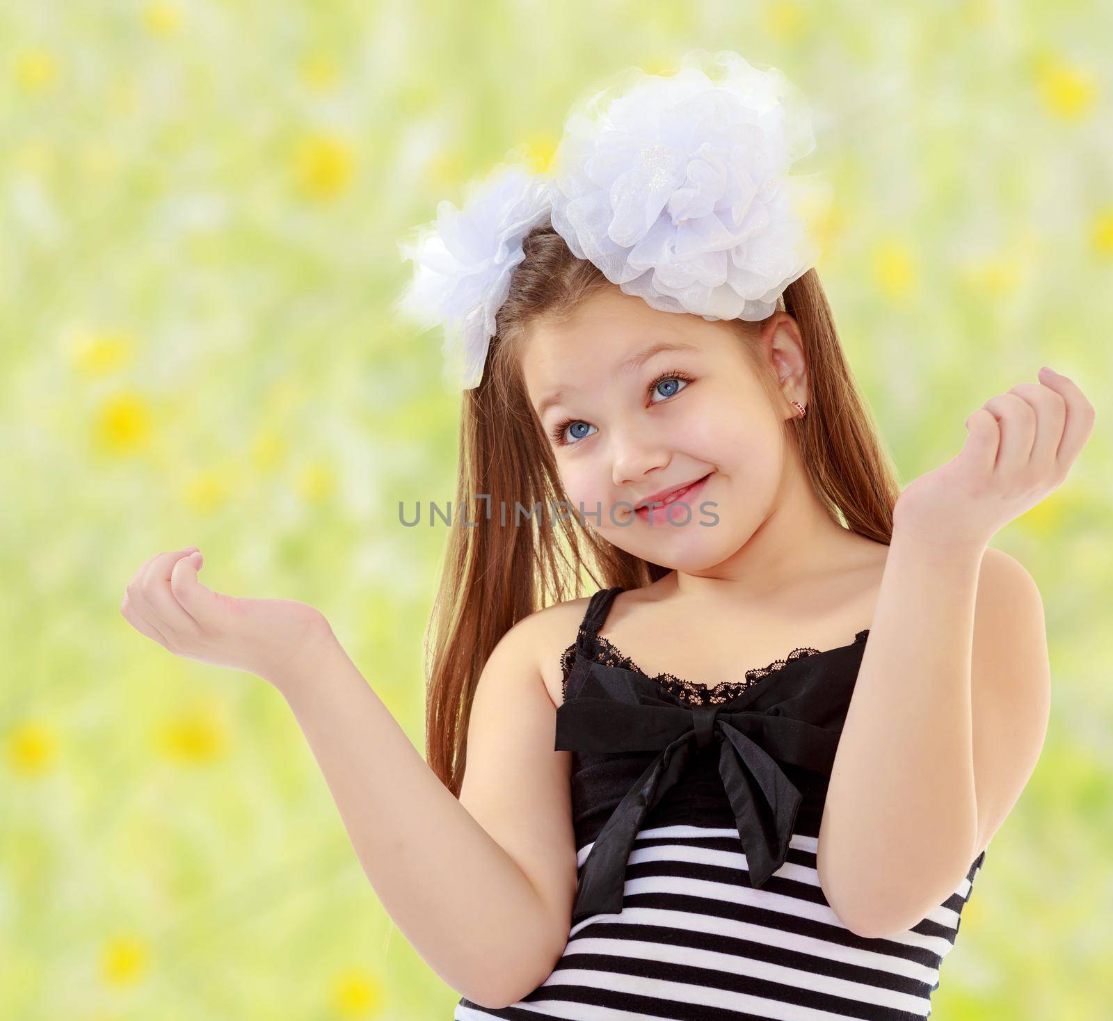 Beautiful, chubby, long-haired little girl with big white bows on the head . girl gesturing with his hands. Close-up.Summer blurred green background with yellow flowers.