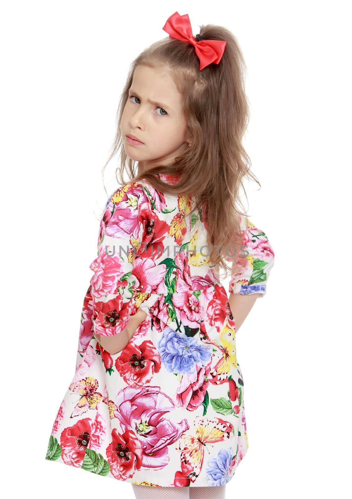 Gentle little girl with a long ponytail down to his shoulders, and a red bow on her head, in a beautiful summer dress. The girl made a serious face. Close-up - Isolated on white background