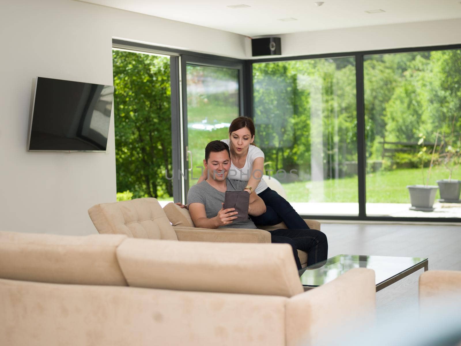 Young couple relaxing at luxurious home with tablet computers reading in the living room on the sofa couch.