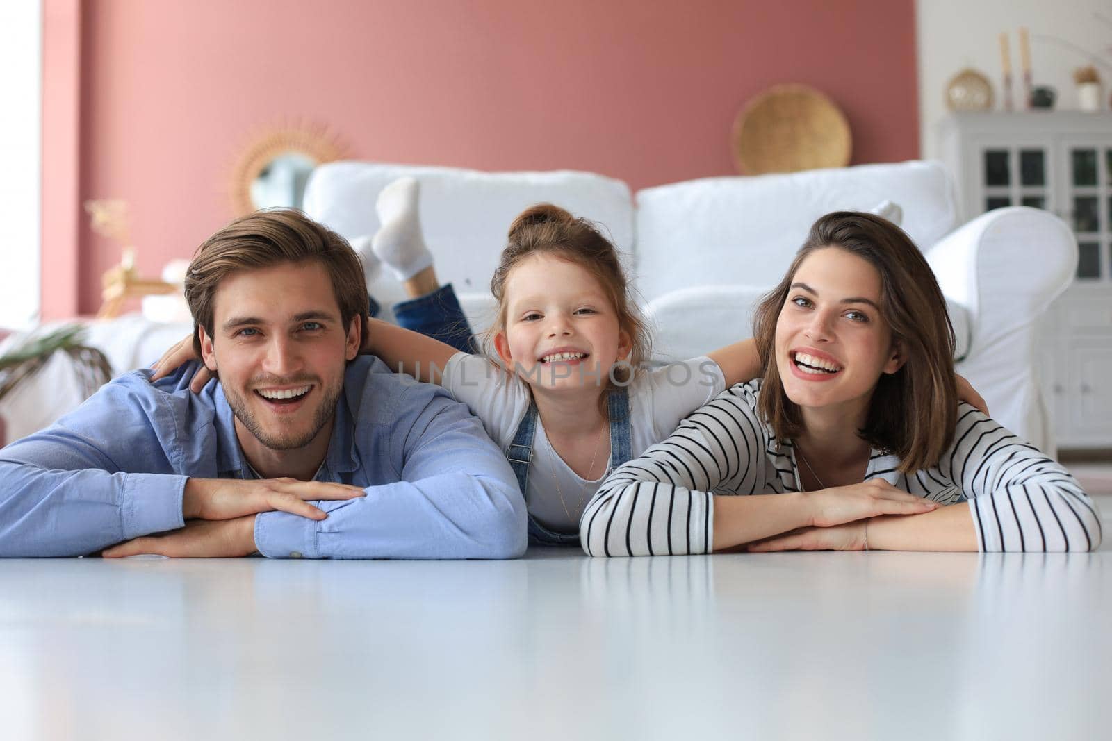 Young Caucasian family with small daughter pose relax on floor in living room, smiling little girl kid hug embrace parents, show love and gratitude, rest at home together