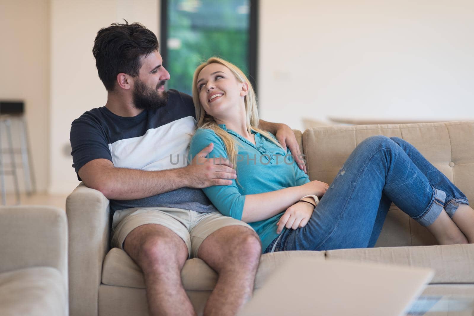 Young couple relaxes on the sofa in the luxury living room, using a laptop and remote control