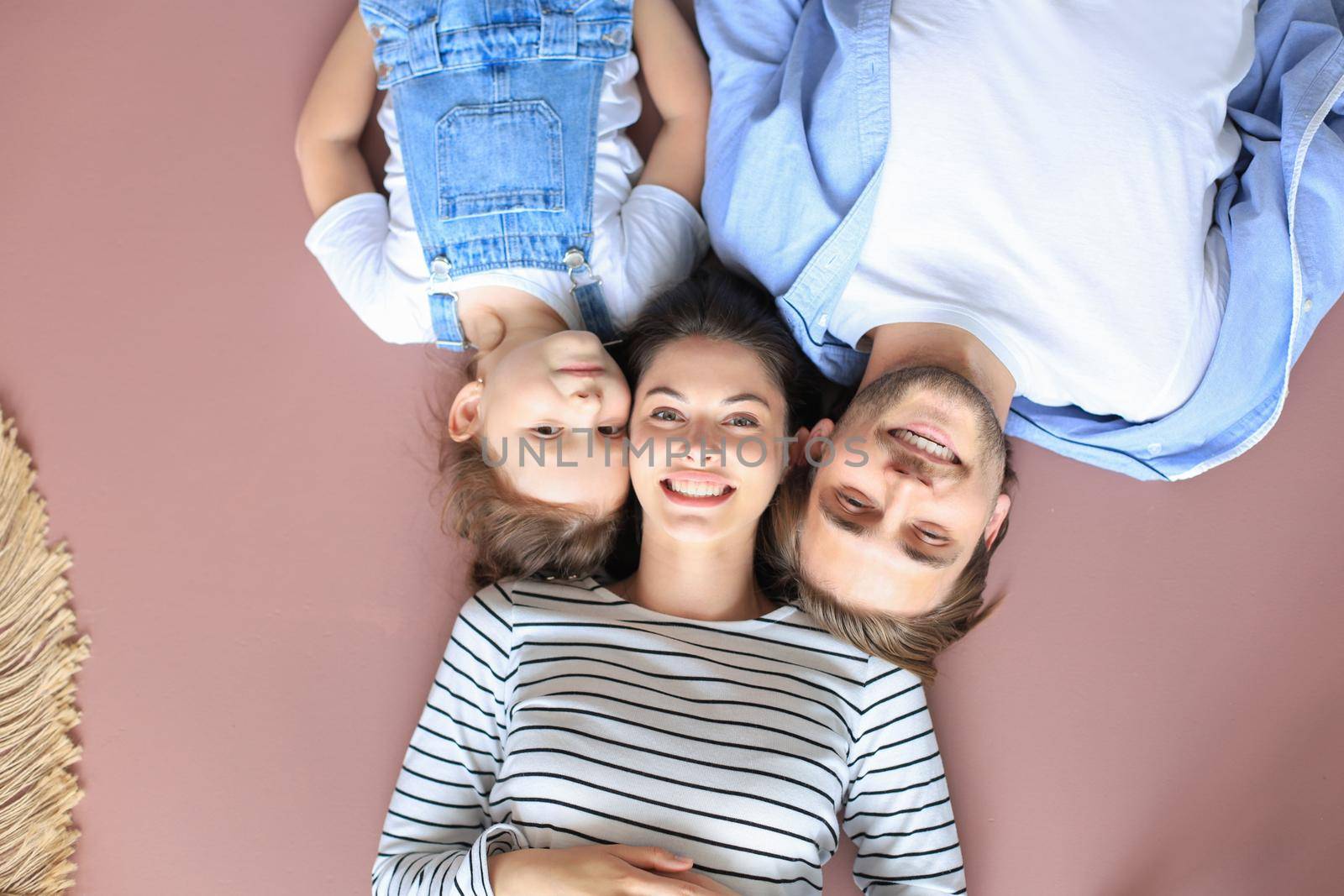 Top view portrait of smiling young parents with little preschooler daughter lying relaxing on warm floor at home, happy family with small child rest have fun at home