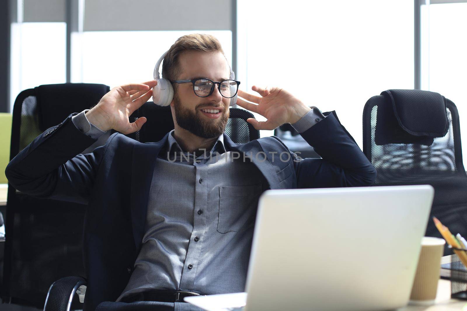 Smiling handsome businessman relaxing and listening music in earphones in a modern office