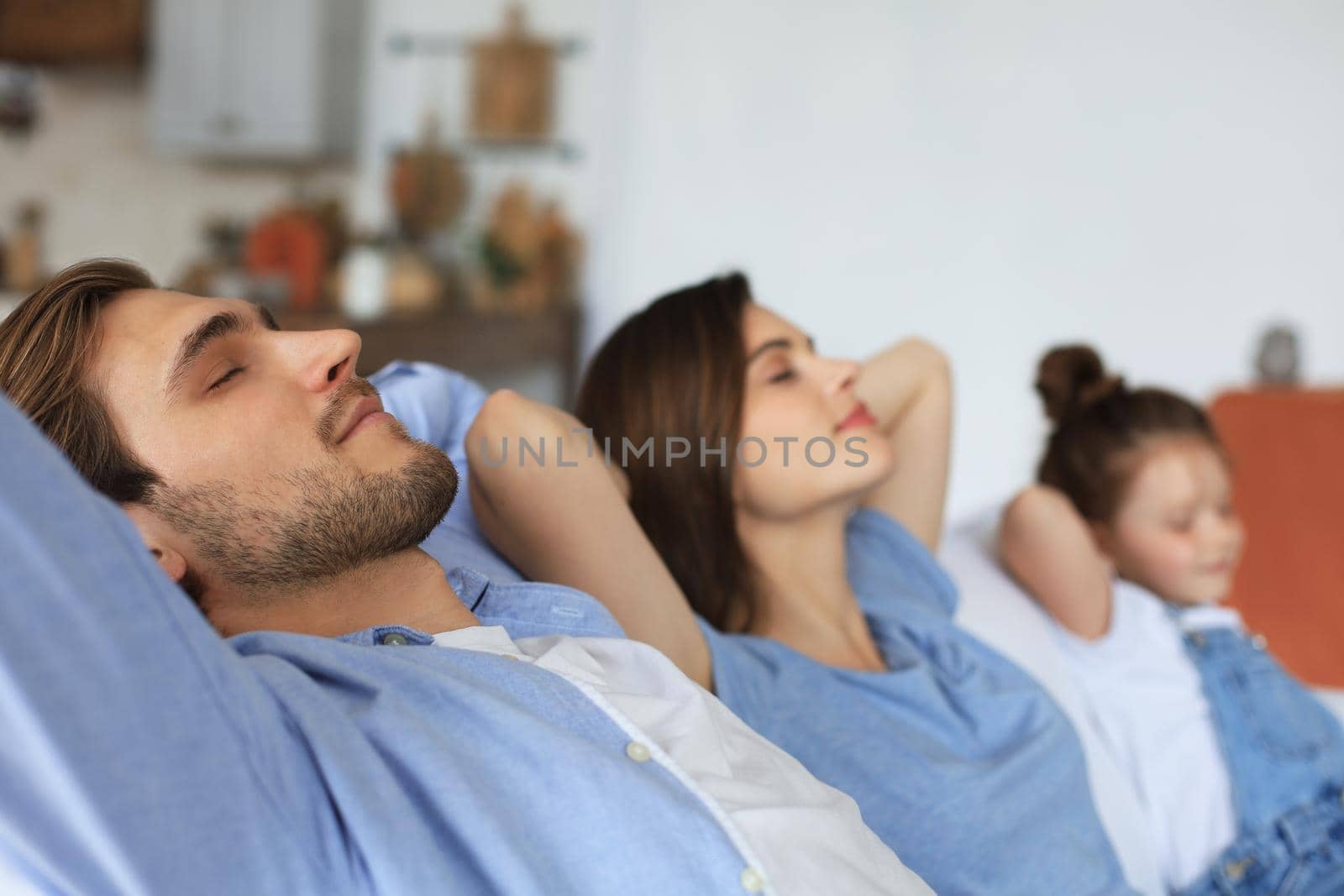 Relaxed young family resting and dreaming about new home on comfortable sofa together at home, happy young parents with little daughter relax enjoying nap relaxing or meditating