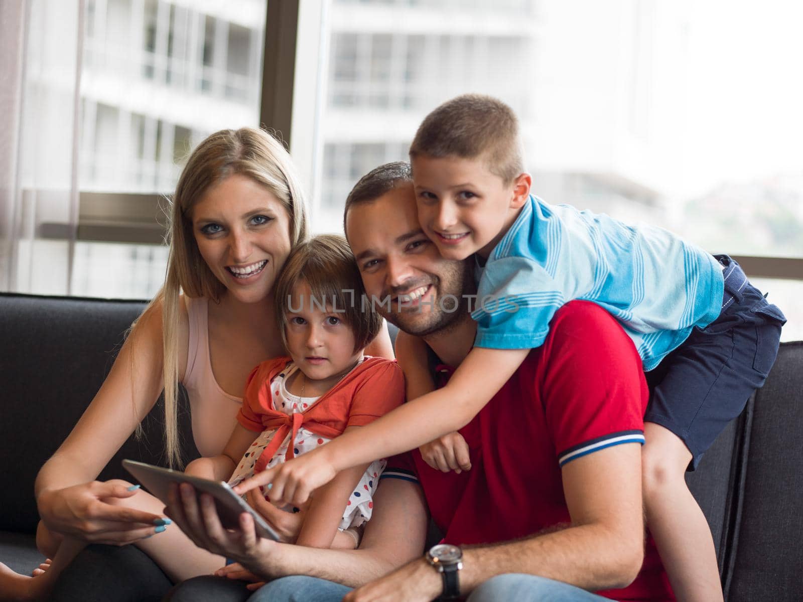 Happy Young Family Playing Together with tablet at home sitting on the sofa