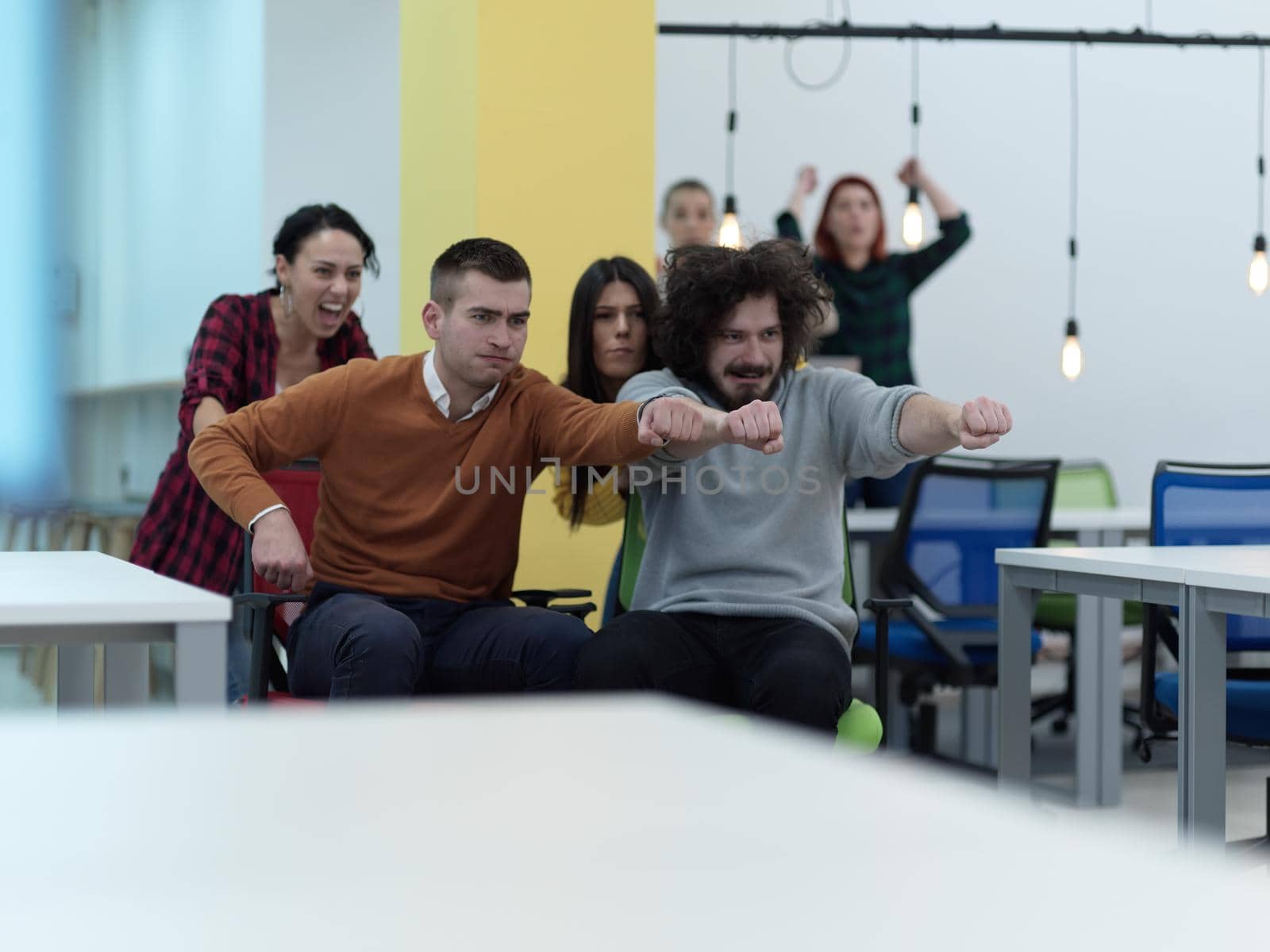 business people having fun while racing on office chairs in modern coworking open space office