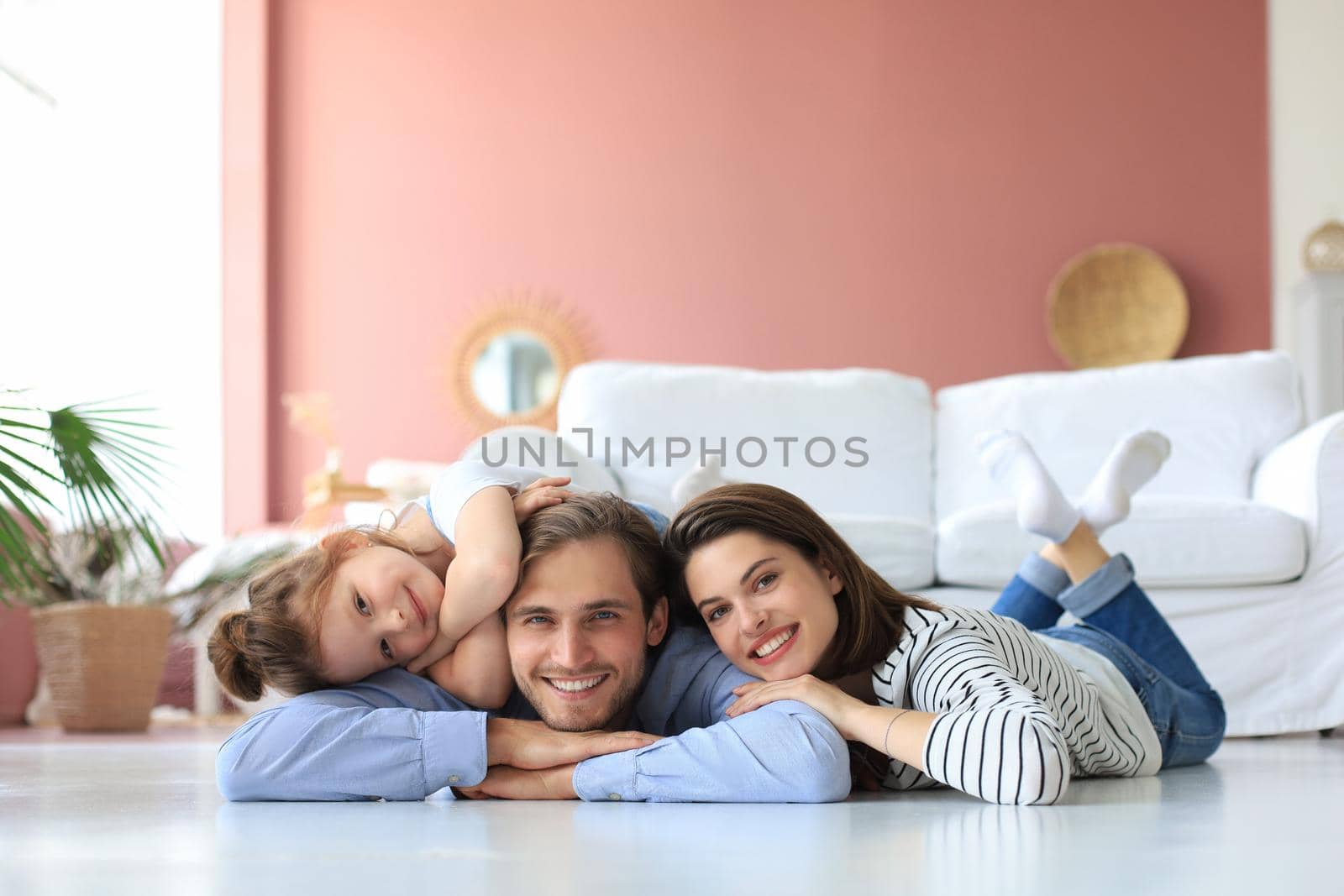 Young Caucasian family with small daughter pose relax on floor in living room, smiling little girl kid hug embrace parents, show love and gratitude, rest at home together