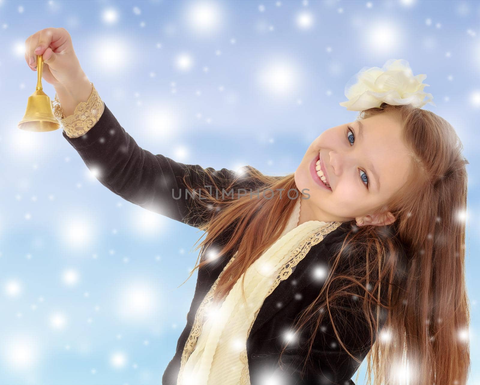 Joyful little long-haired girl with a white rose in her hair, rings the bell. Close-up.Blue Christmas background with white snowflakes.