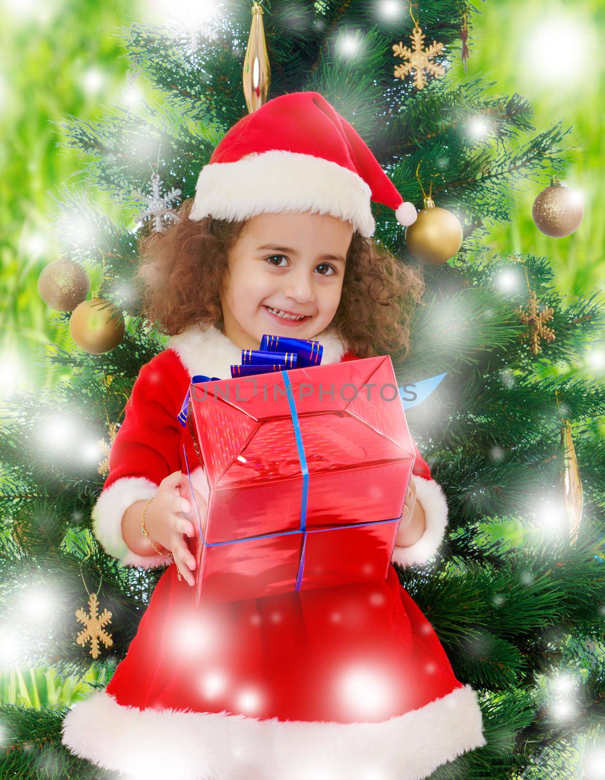 Little girl near the Christmas tree with a gift in its hands by kolesnikov_studio