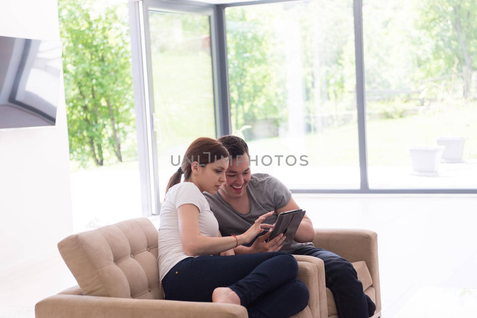 Young couple relaxing at luxurious home with tablet computers reading in the living room on the sofa couch.