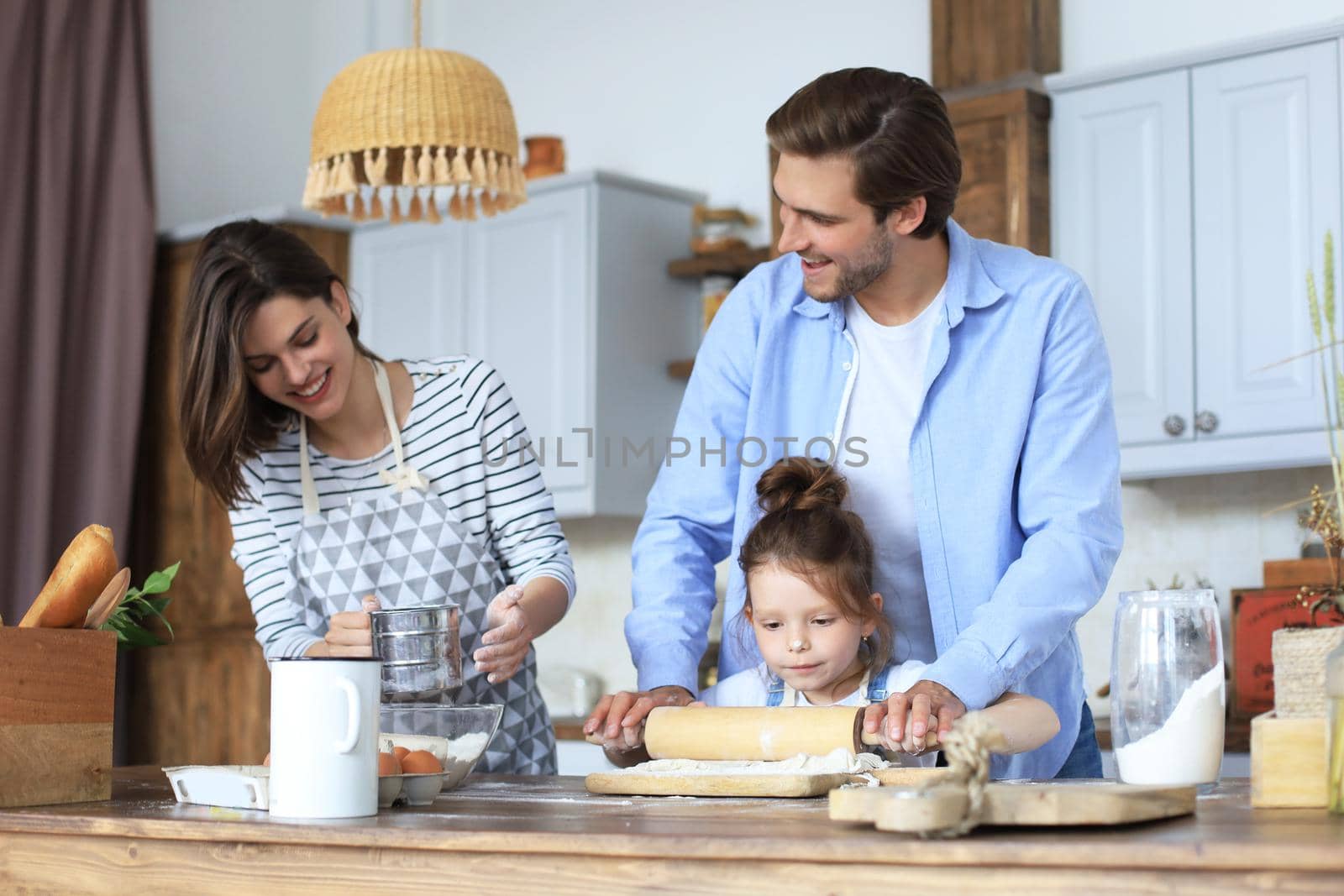 Cute little girl and her parents are having fun while cooking in kitchen at home together. by tsyhun