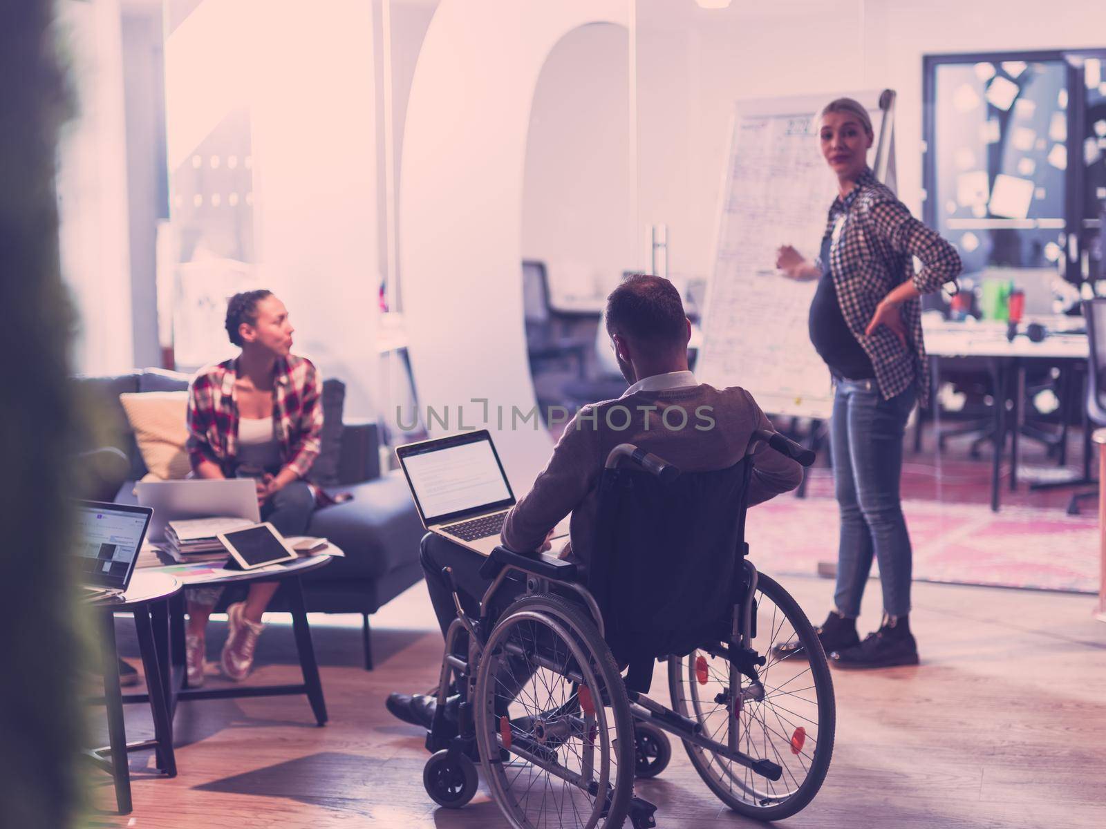 Pregnant Businesswoman Leads Creative Meeting Of Diverse Business Team In Modern Coworking Open Space Office, Disabled coworker in wheelchair attending training 